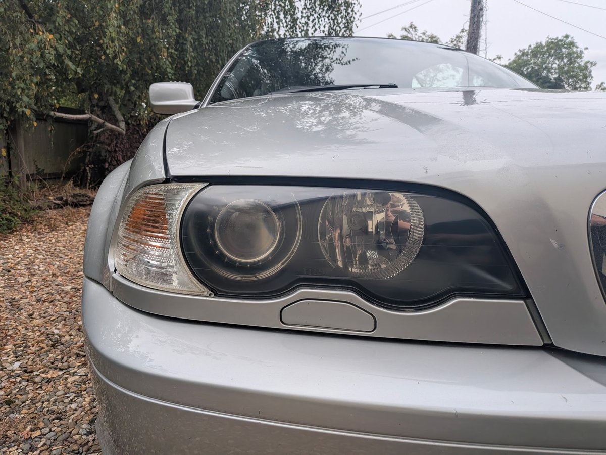 Close-up of a silver sedan's headlight and front bumper against a garden background
